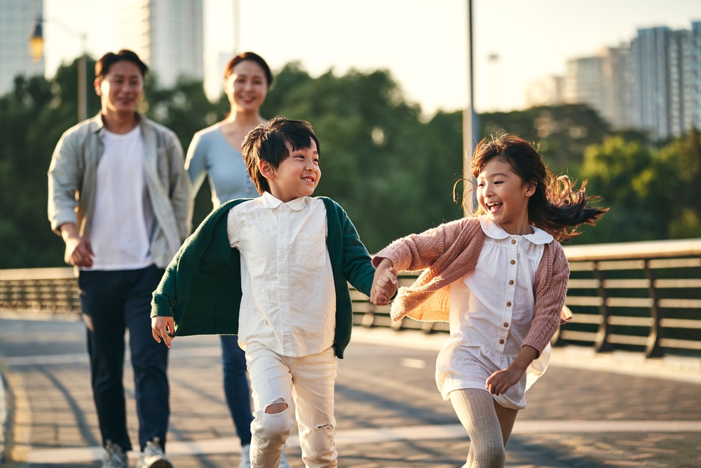 Happy Asian Family With Two Children Walking On Pedestrian Bridge
