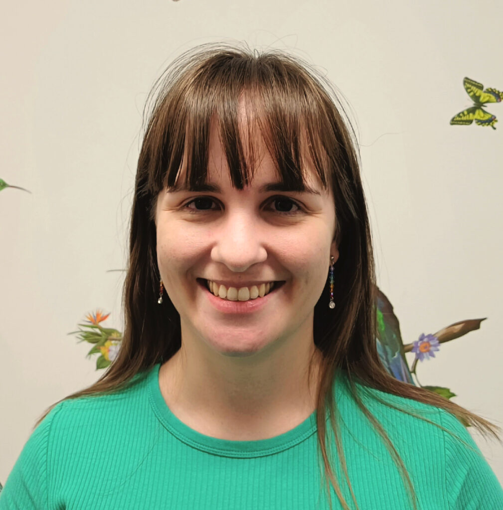 Image of Jo Woolcock, Graduate Speech Pathologist. Young female adult, smiling at camera, she has long, straight hair and a fringe, wearing a bright green crew neck t-shirt.